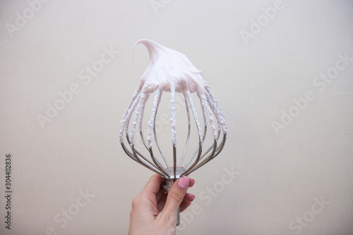 Stainless steel whisk with whipped cream in woman's hand. 
