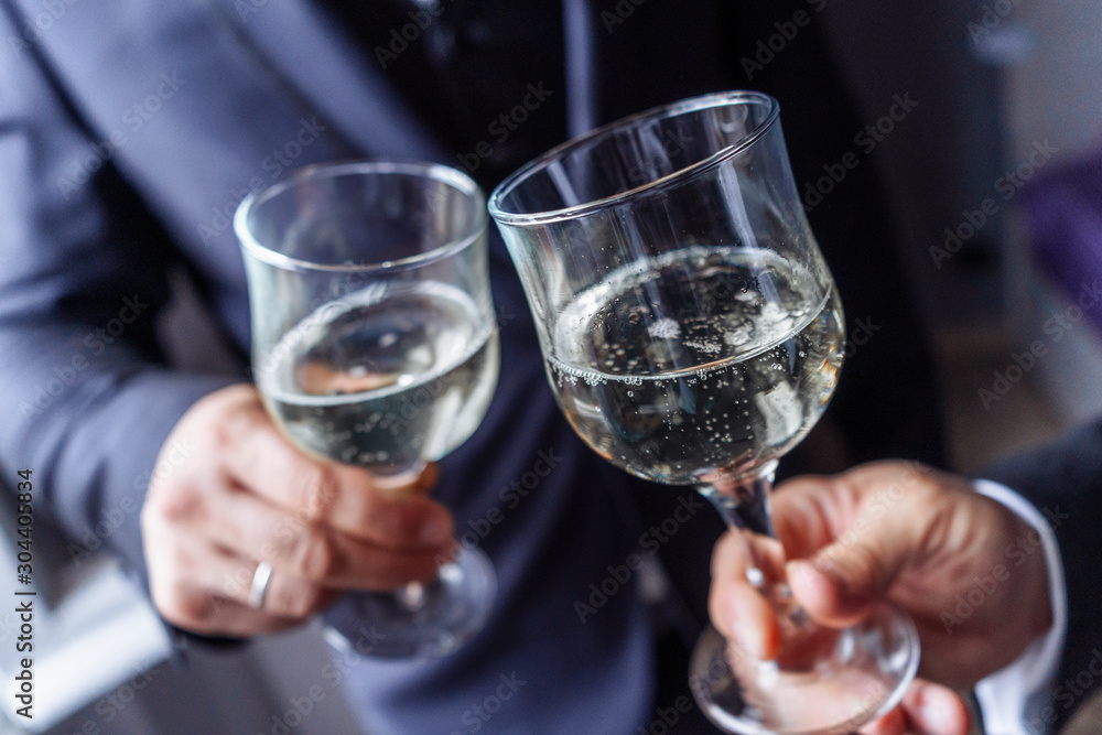 Close up portrait of a male's hands toasting with glasses of wight wine over table