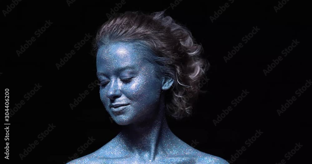 girl with a blue face in sparkles close-up against a black wall looks at the camera girl with a blue face in sparkles close-up against a black wall looks at the camera