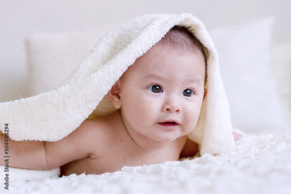 Cheerful cute baby looking at camera under white blanket looking at something. Innocence baby crawling on white bed with towel on his head at home. Cheerful cute baby looking at camera under white blanket looking at something. Innocence baby crawling on white bed with towel on his head at home.