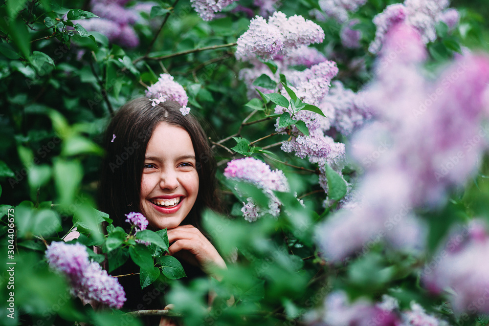 Portrait of a little girl of European appearance against the background of a bush of blooming lilacs in spring. A happy mood in spring Portrait of a little girl of European appearance against the background of a bush of blooming lilacs in spring. A happy mood in spring