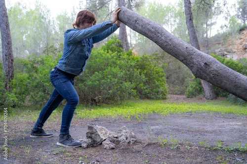 Young caucasian man lifting up a tree trunk in the middle of a forest in Mallorca (Spain)