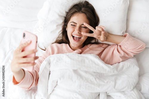 Cheerful lovely young girl wearing pajamas laying in bed