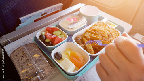 Obraz na plátně Lunch in plane: bread, meat with vegetables and rice, pieces of cheese, dried apricot, salad and beverage in cup