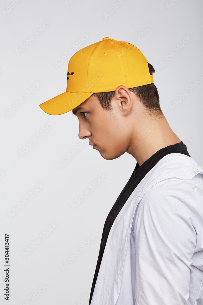 Cropped side photo of a dark-haired man, wearing yellow baseball cap with lettering 