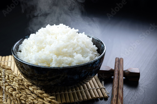 Cooked jasmine rice in ceramic cups and chopsticks and Ear of rice Placed on a black wooden table. Close up shot. 45 degree angle. photo