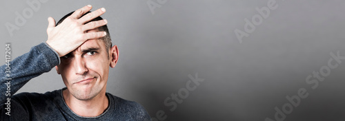 confused young man holding his head, having regret, grey banner photo