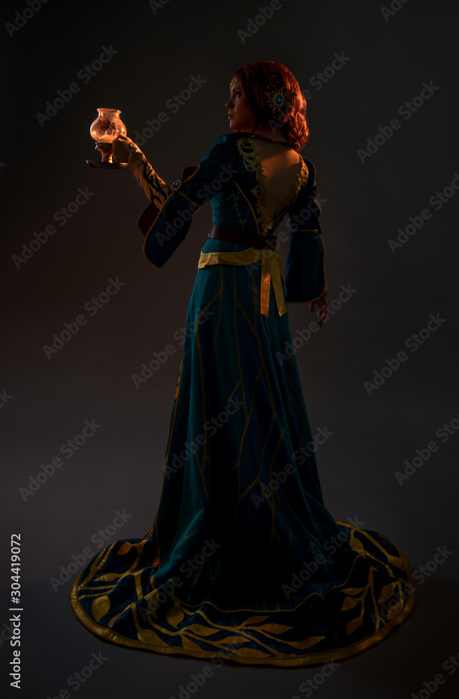 Beautiful redhead woman in cosplay costume with magic lamp on grey background