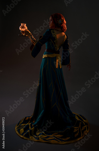 Beautiful redhead woman in cosplay costume with magic lamp on grey background