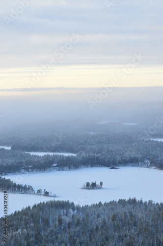 Finnisht winter, Kuusamo. Landscape from Konttainen. Fading daylight, colorful horizon and frozen lakes. Mist descends over the forested hills.