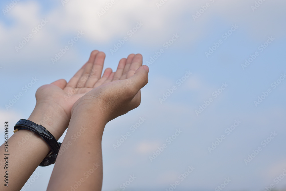 Children's open hands praying for blessing from god over blue sky background.