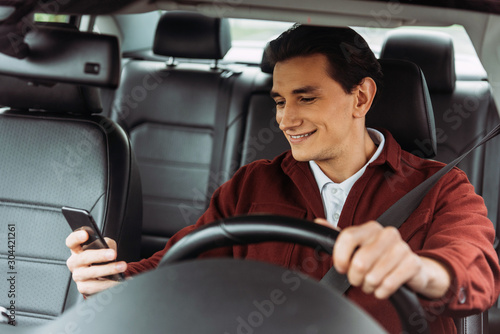 Smiling man looking at smartphone while driving car © LIGHTFIELD STUDIOS