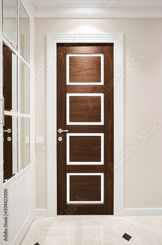 The door is made of walnut wood in a classic style with white architraves in the hallway