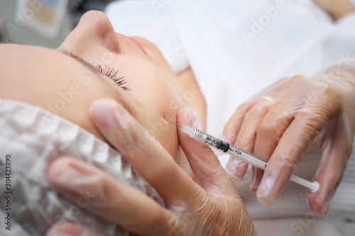 doctor-cosmetician adds missing volume to cheekbones injecting gel-like medicine under skin selective focus
