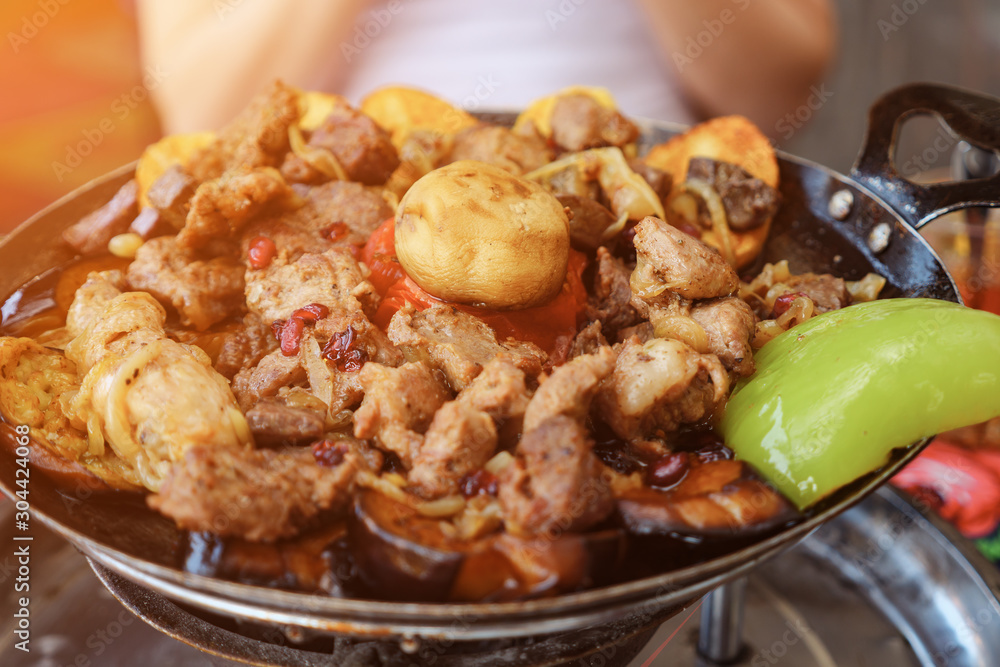 Traditional azerbaijan cuisine food in the restaurant. Woman is eating meat with vegetables served in frying pan, close up. Traditional azerbaijan cuisine food in the restaurant. Woman is eating meat with vegetables served in frying pan, close up.