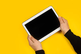 Manos de hombre sosteniendo una tableta sobre fondo amarillo aislado. Vista superior y de cerca. Copy space