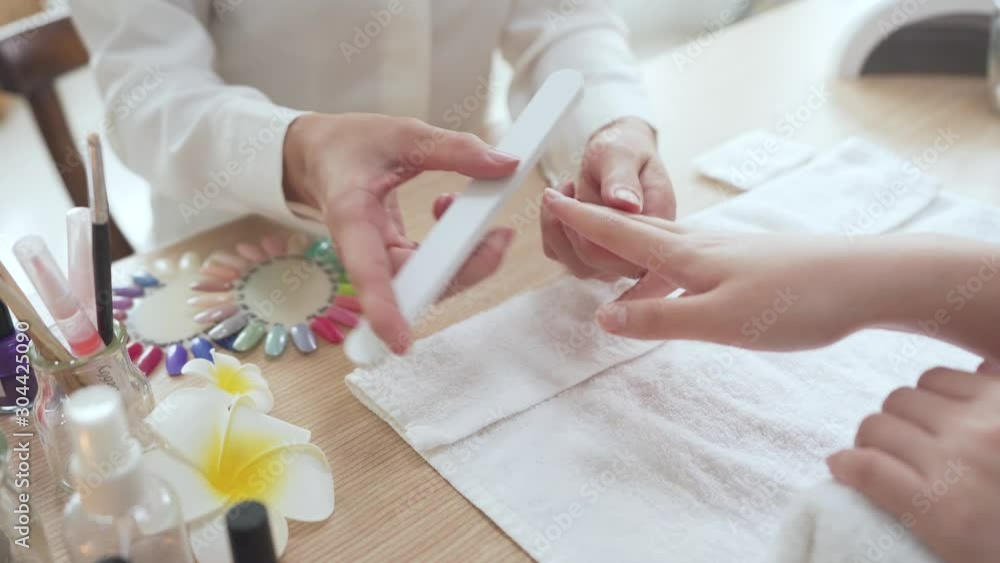 female manicurist doing nail rub by using shiner file tool for woman client in home service. beauty and fashion concept. beautician polishing customer nails with buffer at table indoors. female manicurist doing nail rub by using shiner file tool for woman client in home service. beauty and fashion concept. beautician polishing customer nails with buffer at table indoors.
