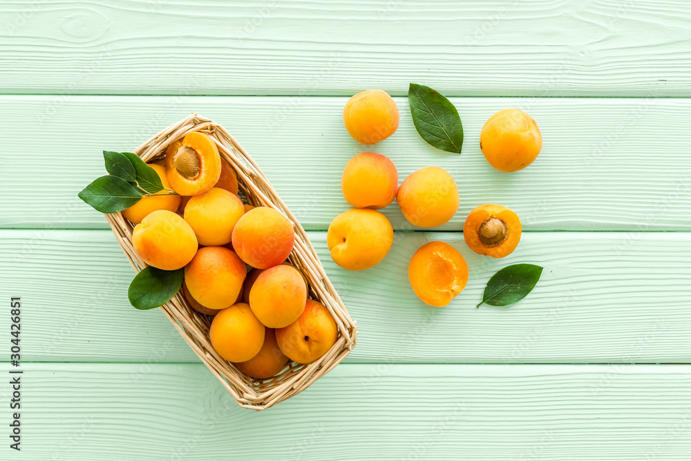 Fresh raw apricots in basket on green wooden background top view pattern with leaves Fresh raw apricots in basket on green wooden background top view pattern with leaves