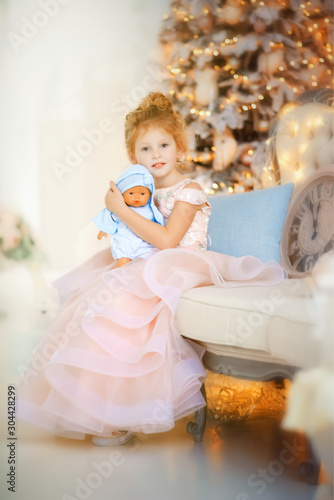 5 years old girl in beautiful light pink dress with doll in blue clothes in christmas time