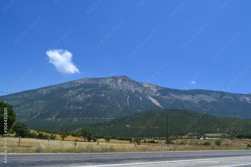 Fototapeta premium The hills and mountains captured from a side of road. Captured in daytime, there is some clouds and blue sky on background.