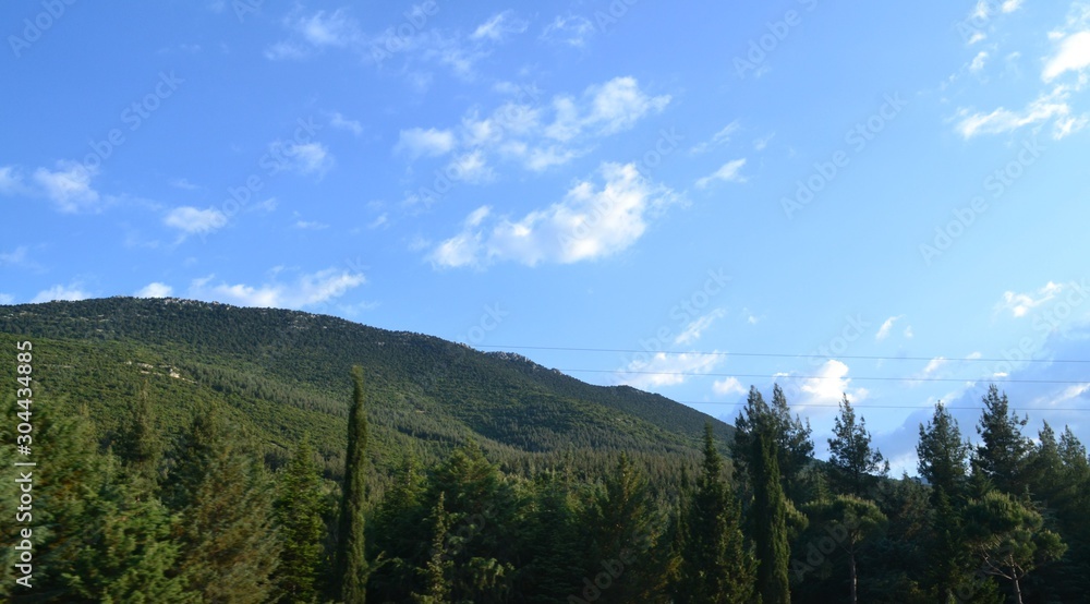 The hills and mountains captured from a side of road. Captured in daytime, there is some clouds and blue sky on background.