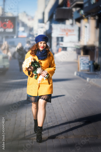 Stylish woman with roses and red lipstick in bright yellow coat and blue hat