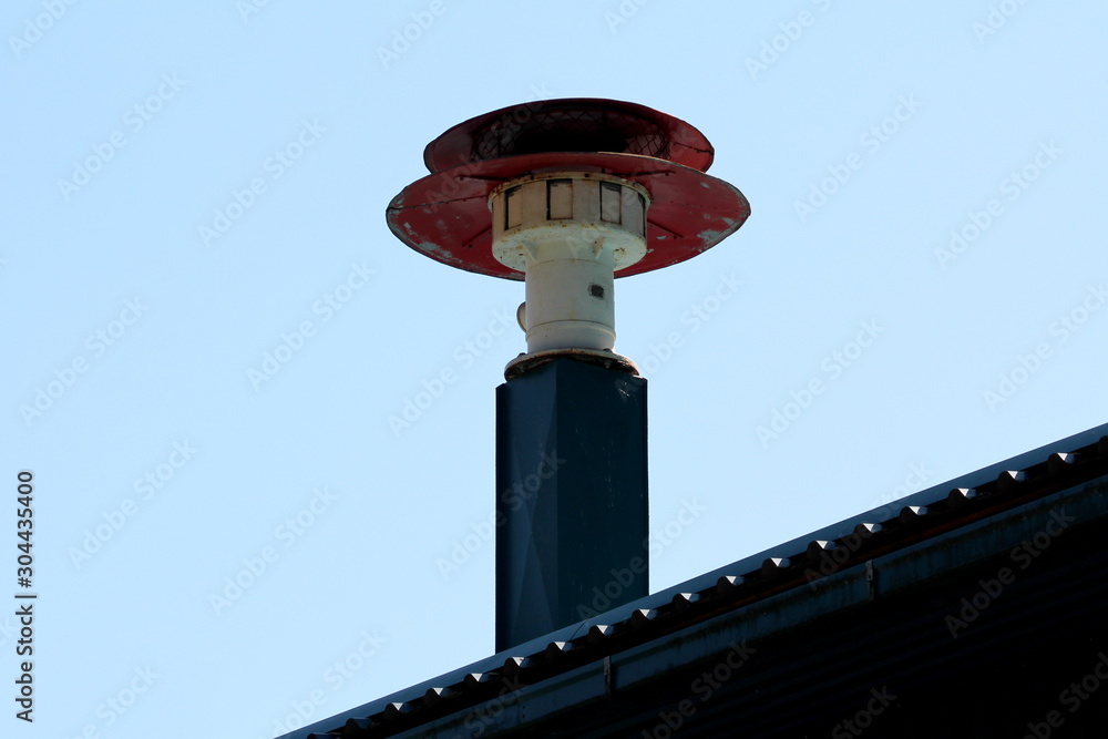 Old vintage retro red and white dilapidated firehouse siren mounted on top of metal column on new roof with clear blue sky in background