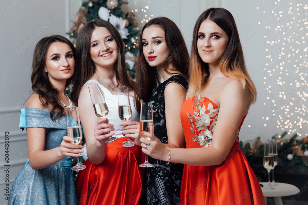 Gorgeous girls In stylish sexy party dresses holding glasses with champagne. Christmas fun. Smiling young girls with professional make up and hairstyle. New year concept. 