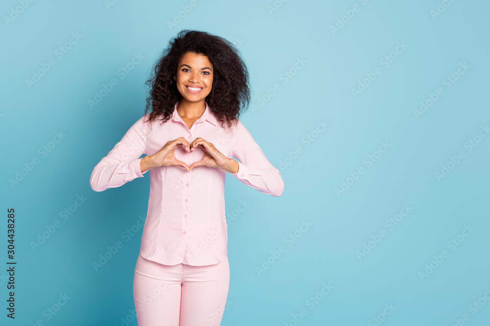 Obraz premium Photo of pretty dark skin wavy lady making heart figure symbol with hands cardiology protection safety wear pink shirt trousers isolated blue color background