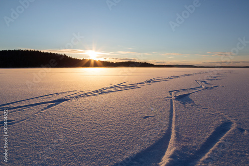 Zig-zag traces of ice-skates on pure snow-covered surface of the lake at beautiful sunset.