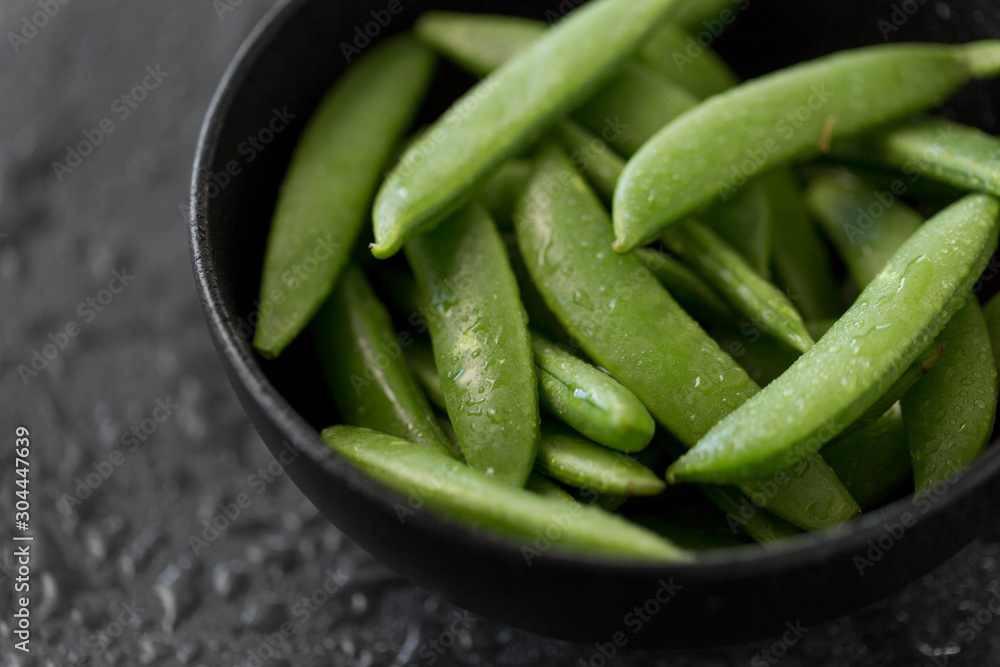 vegetable, food and culinary concept - close up of peas in bowl on wet slate stone background vegetable, food and culinary concept - close up of peas in bowl on wet slate stone background