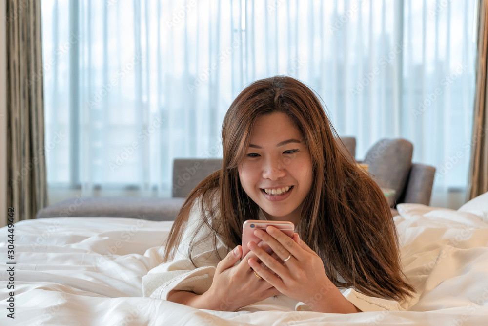 Asian woman in bathrobe suit using smartphone with feeling happy on a bed Asian woman in bathrobe suit using smartphone with feeling happy on a bed