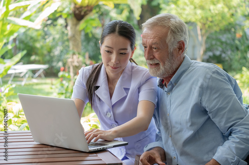 Young nurse take care senior man at home, Senior man with nurse are checking health results online by laptop, Health care concept photo