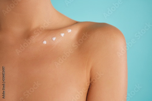 Close up young woman with points of cream on clavicle posing over colorful background isolated