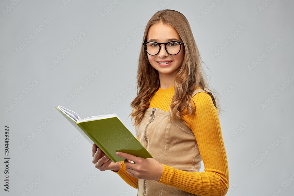 high school, education and vision concept - smiling teenage student girl in glasses reading book over grey background high school, education and vision concept - smiling teenage student girl in glasses reading book over grey background