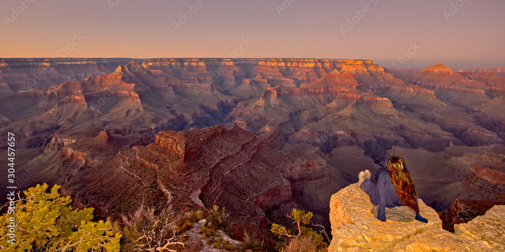 A young woman sitting on the edge of a cliff looking out at the vastness of the Grand Canyon from Shoshone Point at twilight. Woman is facing away from camera. No model release is needed.