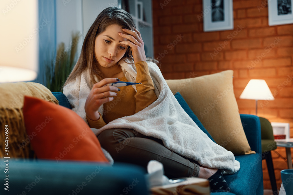 Obraz premium Young woman with cold and flu measuring her temperature