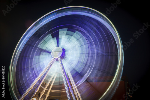 Spinning white purple ferris wheel in motion with black background. An abstract blurred background object image of ferris wheel at night