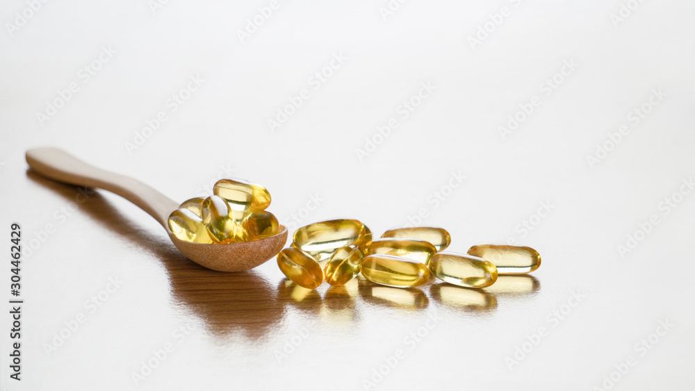 Fish oil capsules with omega3 and vitamin D in wooden spoon on wooden table background,benefits supplement and support heart health,healthy diet concept, selective focus Fish oil capsules with omega3 and vitamin D in wooden spoon on wooden table background,benefits supplement and support heart health,healthy diet concept, selective focus