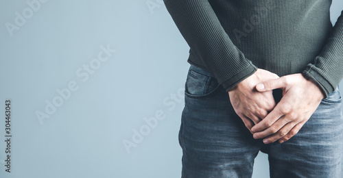 Man holding his urethra in pain on gray background