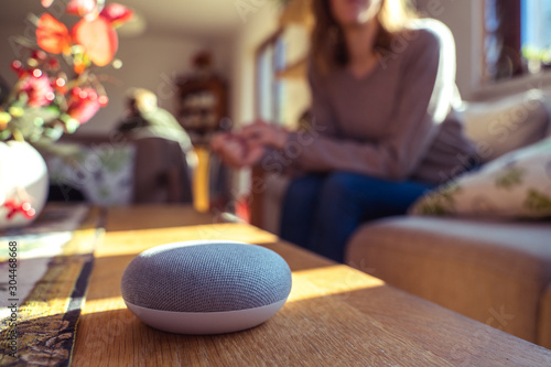 voice controlled smart speaker with a woman woman in the background in a interior home environment. Smart AI speaker concept 