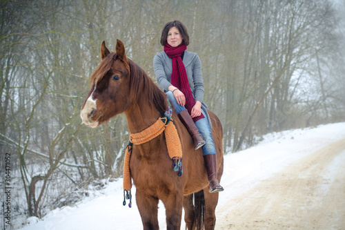 portrait of girl riding red trakehner stallion horse with scarf in winter