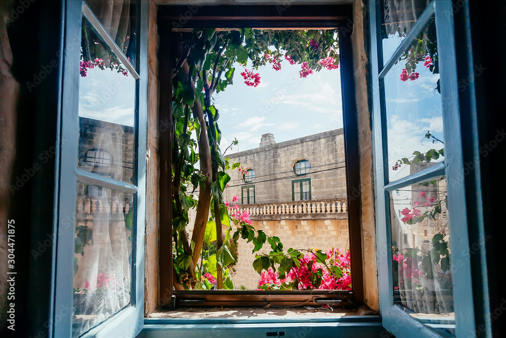Fototapeta View from old house window with garden flowers and historical building behind. Romantic holidays concept