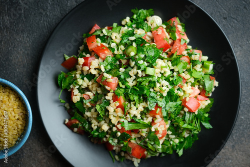 Traditional oriental salad Tabbouleh with bulgur and parsley on a dark background top view copy space.