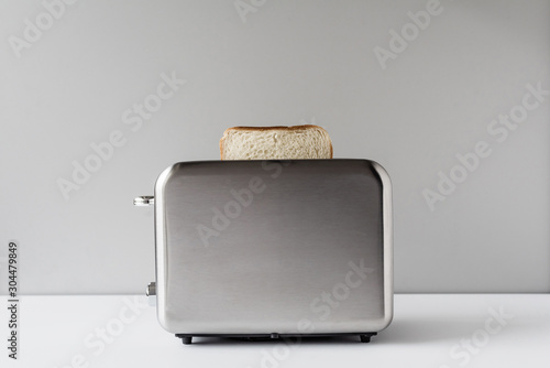 Roasted toast bread popping up of stainless steel retro toaster for breakfast preparation on a gray background.