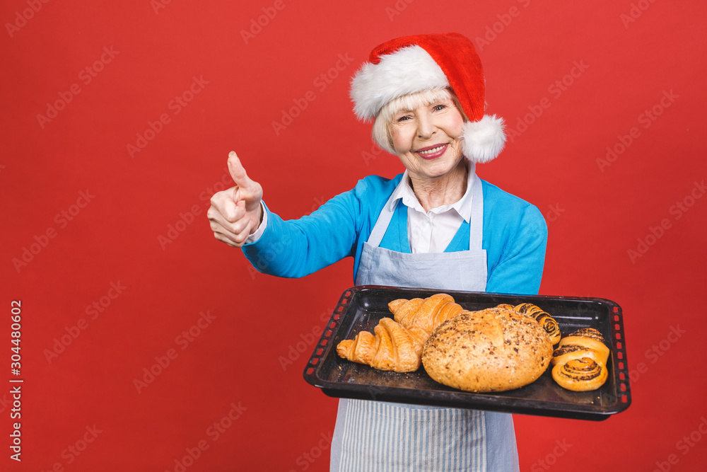 Portrait of pretty charming cheerful aged woman with wrinkle showing gesturing sweet homemade bakery products isolated on red background, christmas recipes. Portrait of pretty charming cheerful aged woman with wrinkle showing gesturing sweet homemade bakery products isolated on red background, christmas recipes.