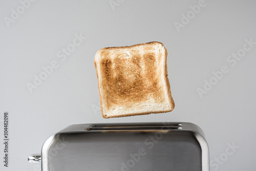 Roasted toast bread popping up of stainless steel retro toaster for breakfast preparation on a gray background.