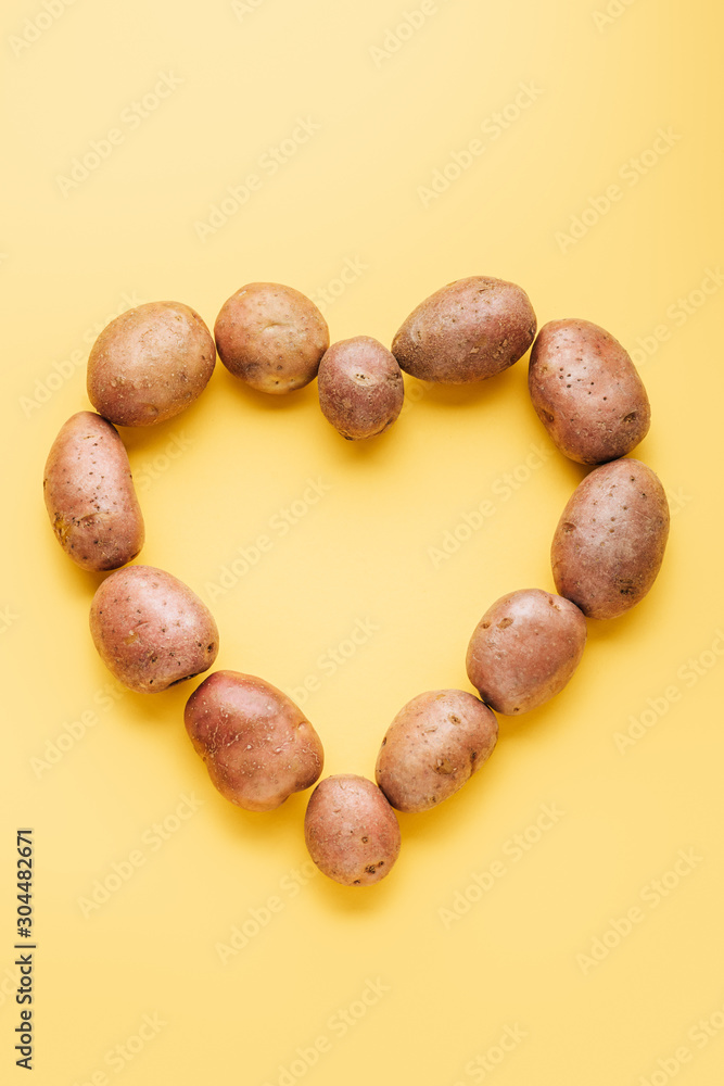 Obraz premium top view of raw whole fresh potatoes arranged in heart on yellow background