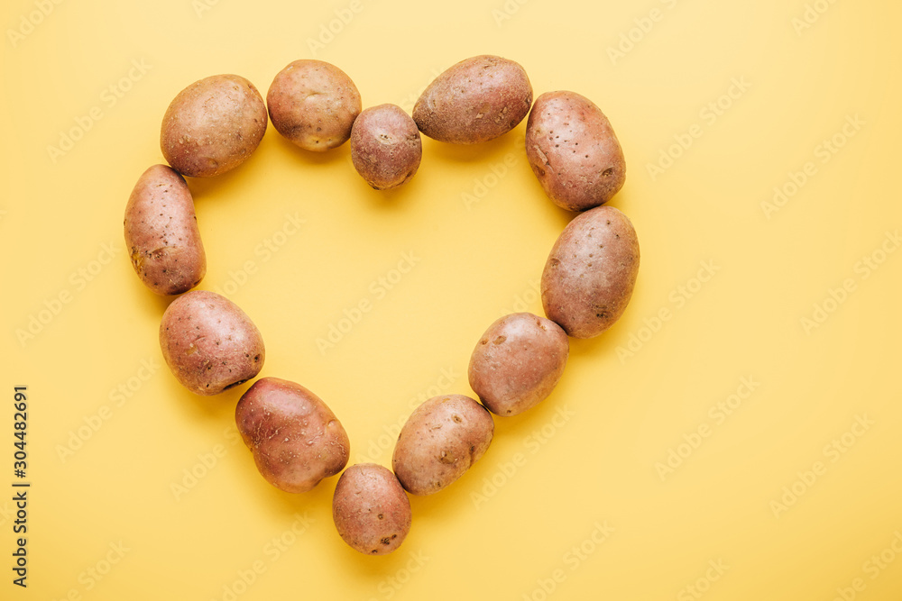 Obraz premium top view of raw whole fresh potatoes arranged in heart on yellow background