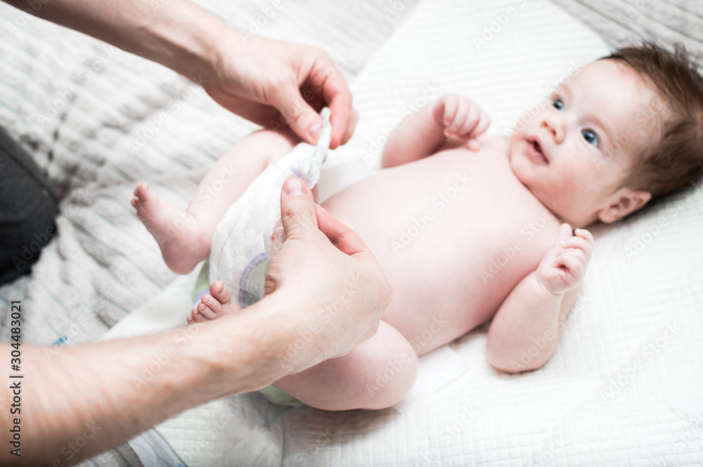 young modern father is caring for his newborn son. Changes the diaper on the bed. Hygiene and newborn care concept. Father's love and care. Father's day. young modern father is caring for his newborn son. Changes the diaper on the bed. Hygiene and newborn care concept. Father's love and care. Father's day.
